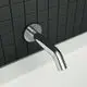 Chromfarbener Wandauslauf von Ideal Standard mit runder Rosette, montiert an einer dunklen Kachelwand über einer weißen Badewanne.